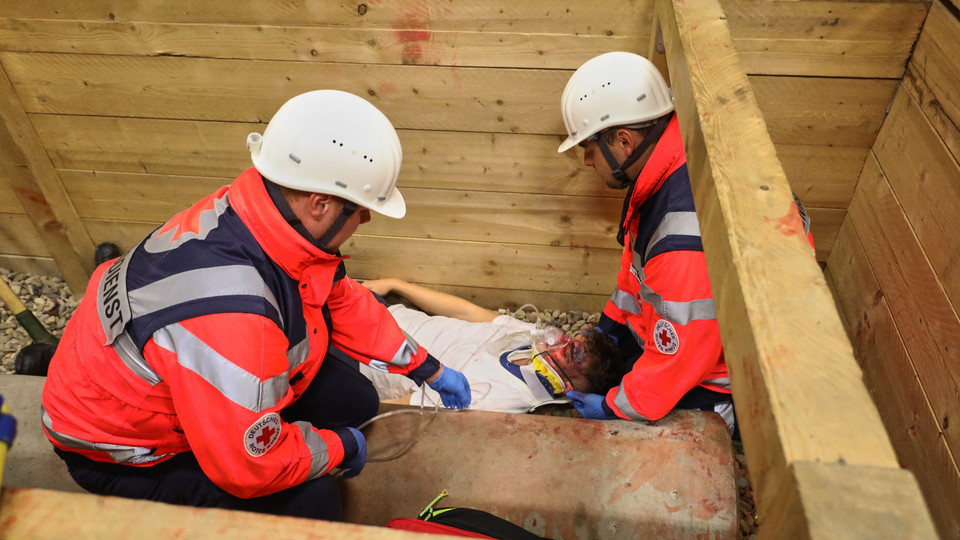 Zwei Rettungskräfte helfen einem verunglückten Arbeiter