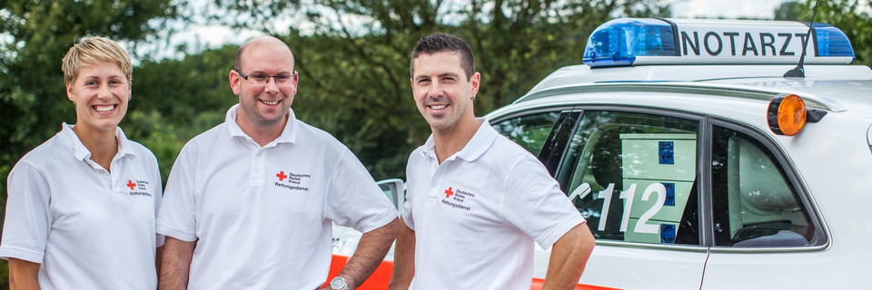 Drei Sanitäter stehen vor einem Rettungswagen